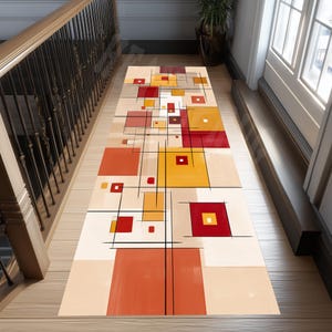 May include: A rectangular runner rug with an abstract geometric design. The rug features squares and rectangles in shades of red, orange, and yellow, with black lines and a beige background. The rug is placed on a wooden floor near a staircase.
