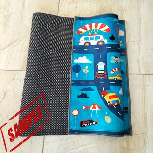 May include: A blue and gray play mat with a colorful design featuring cars, trucks, and a hot air balloon. The mat has a gray border and a black and white checkered pattern on the left side.