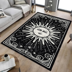 Puede incluir: Alfombra negra y blanca con un diseño de sol y estrellas. El sol tiene una cara y está rodeado de rayos. La alfombra tiene un borde decorativo.
