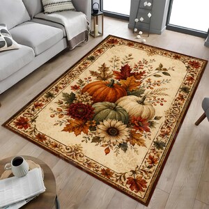 May include: A rectangular area rug featuring a cream-colored background with a decorative border of autumn leaves. The center displays a cluster of orange, green, and white pumpkins, a large sunflower, red dahlias, and various fall foliage.
