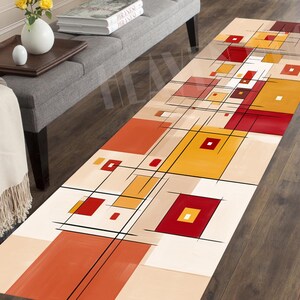 May include: A rectangular area rug with an abstract geometric design. The rug features a beige background with squares and rectangles in shades of red, orange, and yellow, outlined with black lines. The rug is placed on a dark wood floor.