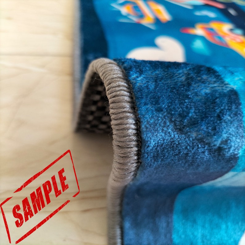 May include: Close-up of a blue rug with a gray border. The rug has a textured surface and a design of abstract shapes.