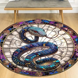 Puede incluir: Una alfombra redonda con un diseño de vitral que presenta una serpiente azul y morada con un ojo rojo. La serpiente está enroscada alrededor de un marco circular con un patrón de vitral.