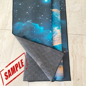 May include: A rolled-up rug with a celestial design featuring a starry night sky and blue clouds. The rug's underside is a gray and white checkered pattern. A red "SAMPLE" stamp is visible.