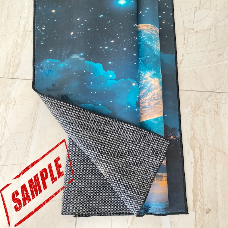 May include: A rolled-up rug with a celestial design featuring a starry night sky and blue clouds. The rug's underside is a gray and white checkered pattern. A red "SAMPLE" stamp is visible.