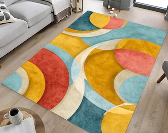 May include: A rectangular area rug with an abstract design. The rug features overlapping shapes in shades of yellow, red, blue, and cream. The rug is placed on a hardwood floor, with a sofa and coffee table visible in the background.