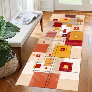 May include: A rectangular area rug with a geometric design. The rug features squares and rectangles in shades of red, orange, yellow, and beige, with black lines. The rug is placed on a wooden floor.