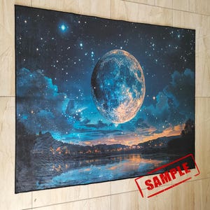 Pode incluir: Uma tape&ccedil;aria retratando uma cena celestial com uma grande lua brilhante no centro. A obra de arte apresenta um c&eacute;u noturno azul escuro cheio de estrelas e nuvens, com um rio e uma cidade distante na parte inferior. A palavra "SAMPLE" est&aacute; carimbada em vermelho.