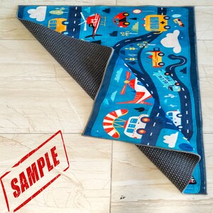 May include: A blue and red children's play rug with a road and vehicles design. The rug features a school bus, a helicopter, a car, and a truck. The rug is rolled up and has a non-slip backing.