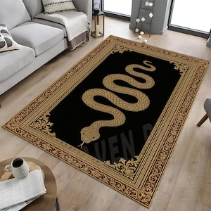 May include: A rectangular rug with a black central panel, displaying a golden snake motif. The rug is framed by a decorative border in gold and brown tones. The word "VEN" is visible at the bottom of the rug.
