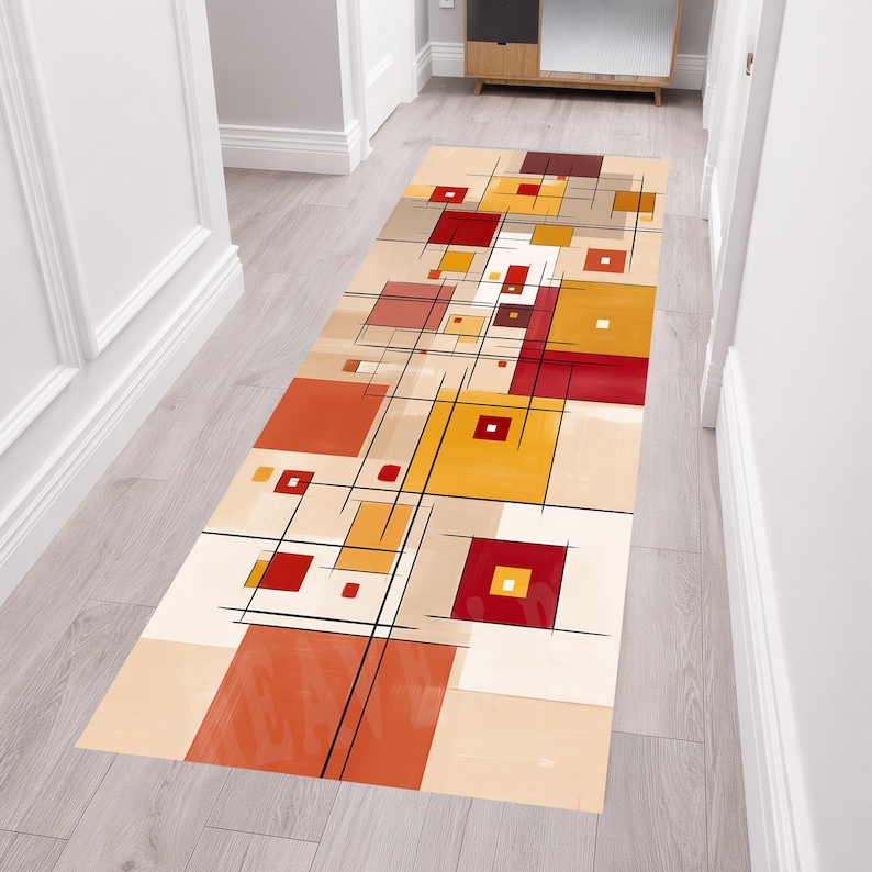 May include: A rectangular hallway runner rug with an abstract geometric design. The rug features squares and rectangles in shades of red, orange, yellow, and beige, with black lines. The rug is placed on a light wood floor.