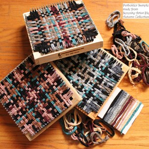May include: Three wooden looms with woven potholders in various colors, including black, brown, teal, and pink. The looms are surrounded by yarn scraps in various colors. The text "Potholder Samples made from Serenity Artist Blend Autumn Collection" is visible in the top right corner.