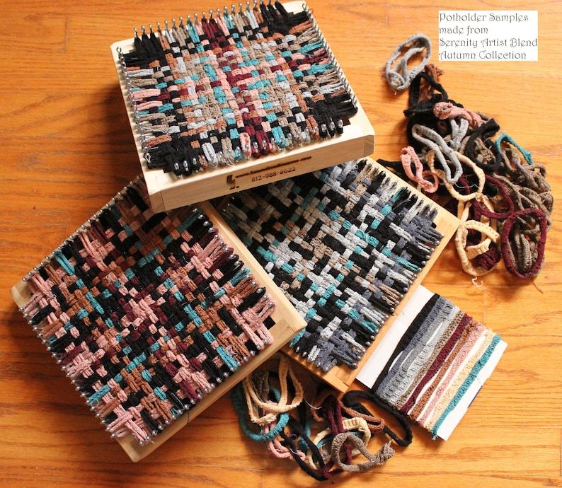 May include: Three wooden looms with woven potholders in various colors, including black, brown, teal, and pink. The looms are surrounded by yarn scraps in various colors. The text "Potholder Samples made from Serenity Artist Blend Autumn Collection" is visible in the top right corner.