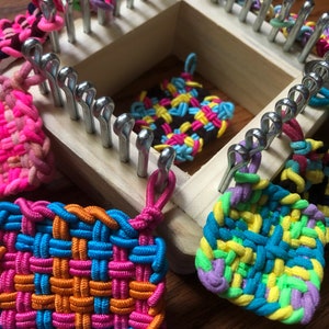 May include: A wooden loom with colorful rubber band bracelets and squares. The loom has metal pegs and is used to create woven bracelets and squares.