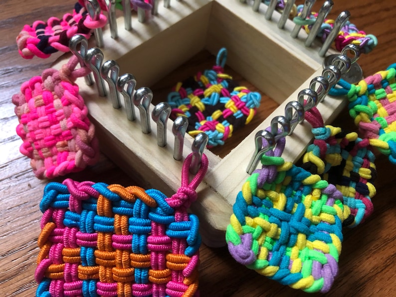 May include: A wooden loom with colorful rubber band bracelets and squares. The loom has metal pegs and is used to create woven bracelets and squares.