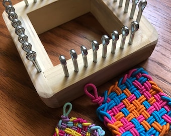 May include: A wooden loom with metal pegs for weaving colorful rubber band bracelets. Two finished bracelets are shown, one with pink, yellow, and purple bands, and the other with blue, orange, and pink bands.