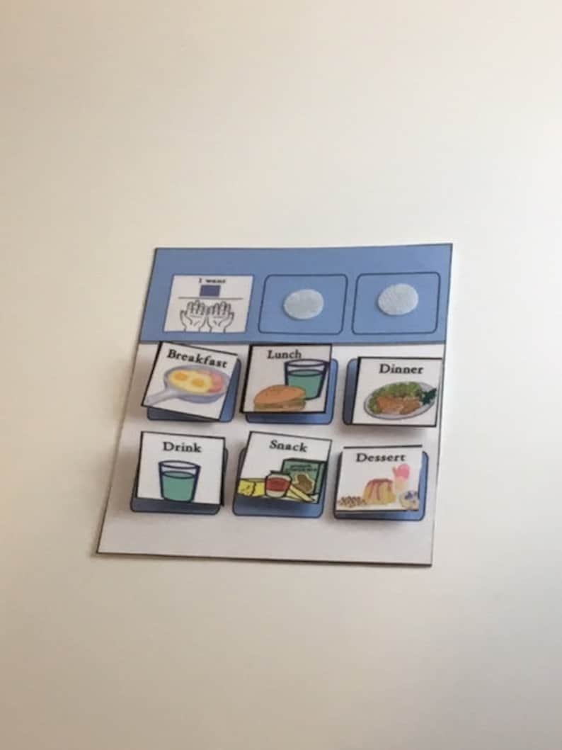 May include: A visual communication board with illustrated meal options. The board includes images for breakfast, lunch, dinner, drink, snack, and dessert. The top section has two blank circles and a section that says "I want" with hand gestures.