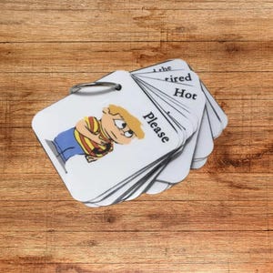 May include: A stack of white flashcards with a metal ring. One card features a cartoon boy with the word "Please". Other cards show the words "the", "tired", and "Hot". The cards are on a wooden surface.