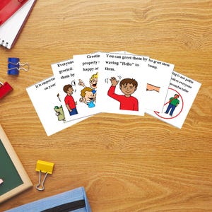 May include: A collection of educational cards with illustrations and text on a wooden surface. The cards feature cartoon figures demonstrating greetings and social etiquette. Text includes phrases like "Everyone greeted" and "You can greet them by waving 'Hello' to them."