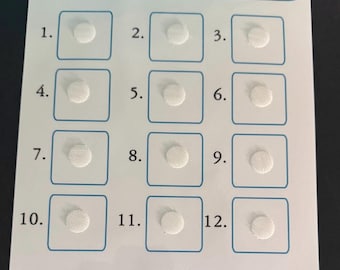 May include: A white card with the text "TIME TO/FOR" at the top, above a grid of twelve numbered squares. Each square contains a small, white, circular patch. The top of the card has three blue rectangles with white circles.