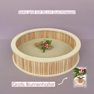 Könnte beinhalten: Ein rundes Holztablett mit vertikalen Stäben an den Seiten und einem beigen Boden, mit dem Text 'Extra groß mit 35 cm Durchmesser!' und 'Gratis Blumenhalter'. Ein kleiner Blumenhalter aus Holz mit der Aufschrift 'Für deinen Liebling' ist enthalten.