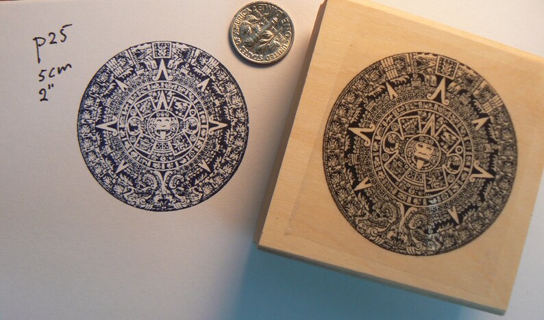 May include: A wooden stamp with a black and white image of the Aztec calendar, also known as the Sun Stone. The stamp is 2 inches in diameter.