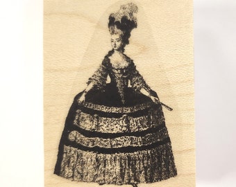 Puede incluir: Un sello de goma negro y blanco montado en madera con una mujer con un vestido grande y de capas y un sombrero de plumas. La mujer sostiene un abanico en su mano derecha.