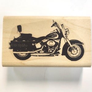 Puede incluir: Sello de motocicleta negra sobre un bloque de madera clara. La motocicleta es una ilustración detallada con asiento, alforjas y faro delantero. Ideal para proyectos de manualidades y scrapbooking.