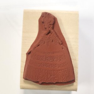 May include: A wooden mounted rubber stamp featuring a detailed silhouette of a woman in a long dress.