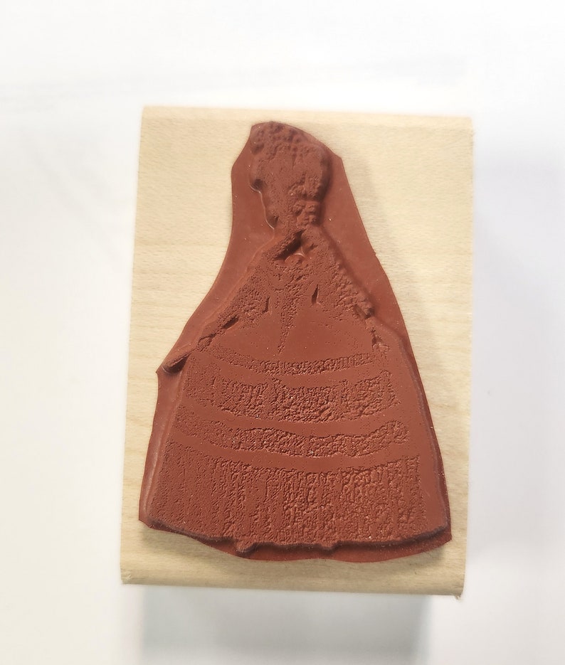 May include: A wooden mounted rubber stamp featuring a detailed silhouette of a woman in a long dress.