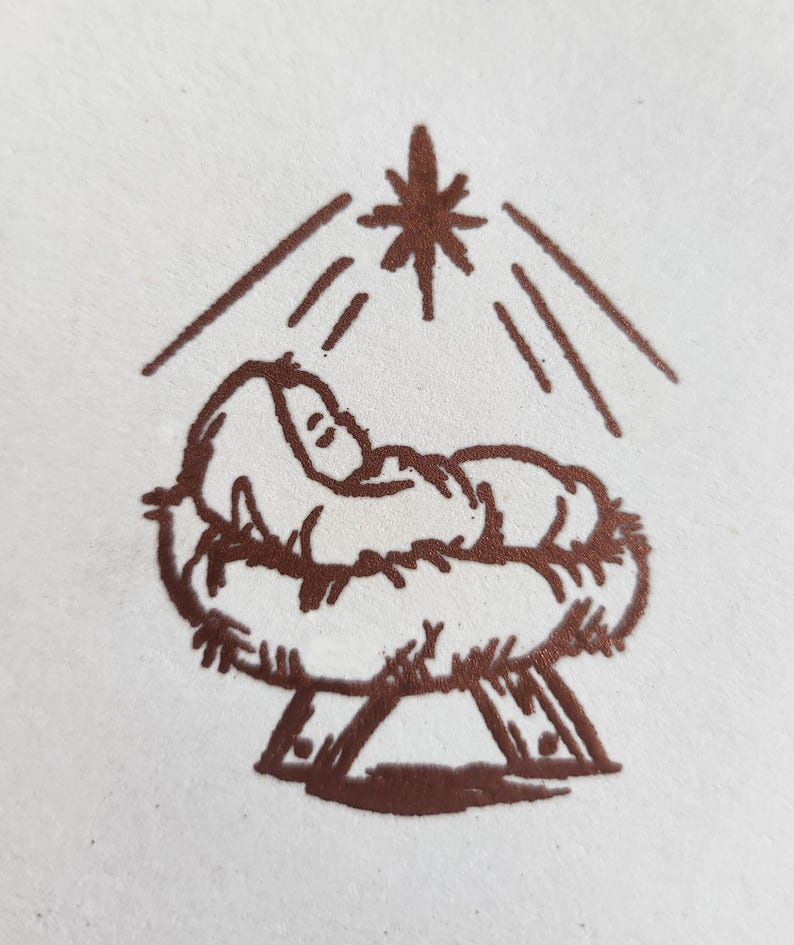 May include: A brown line drawing of a baby in a manger with a star above it.