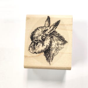 Könnte beinhalten: Ein Holzstempel mit einer Schwarzweißillustration eines Eselskopfes. Der Esel schaut nach links und hat eine flauschige Mähne.