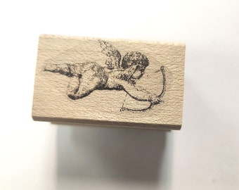 May include: A wooden stamp with a black and white image of a cherub with wings holding a bow and arrow.