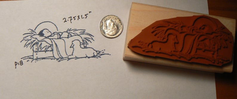 May include: A wooden rubber stamp with a brown rubber image of a nativity scene. The image shows a baby in a manger with a sheep and a star above. The stamp is 2.75 x 1.5 inches.
