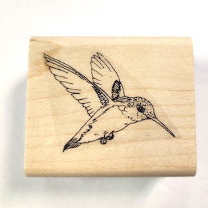 May include: A wooden stamp with a black line drawing of a hummingbird in flight.