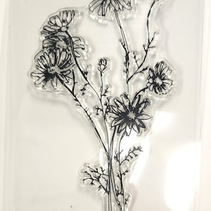 May include: Clear stamp sheet with a design of a bouquet of black and white daisies with stems and leaves.