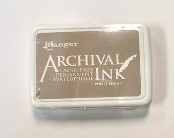 May include: A white ink pad with a brown label that reads "Ranger Archival Ink Acid Free Permanent Waterproof Pebble Beach".