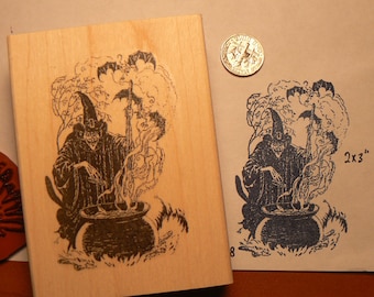 Könnte beinhalten: Ein Holz-Stempel mit einer Schwarzweiß-Illustration einer Hexe, die einen Kessel mit umherfliegenden Fledermäusen umrührt. Der Stempel misst 2x3 Zoll.