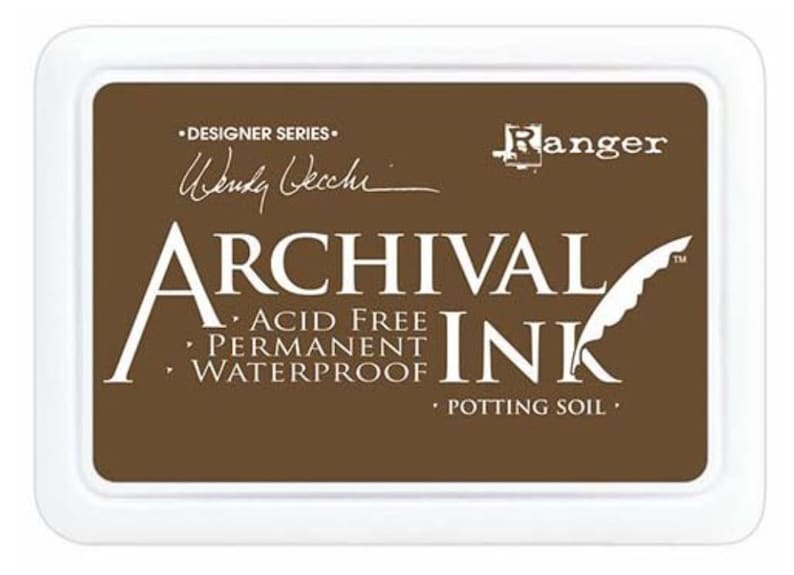 May include: A brown ink pad with the text "ARCHIVAL INK" in white lettering. The ink pad is labeled "ACID FREE, PERMANENT, WATERPROOF" and "POTTING SOIL". The ink pad is from the "DESIGNER SERIES" by Ranger.