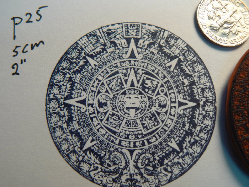 May include: A blue and white circular stamp with an intricate design, featuring a central sun with a face and a ring of glyphs around it. The stamp is 2 inches in diameter and is labeled "P25".