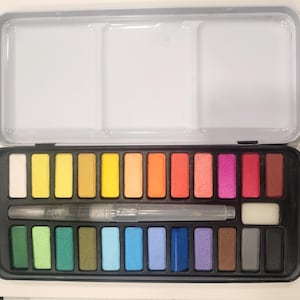 Puede incluir: Un juego de pintura de acuarela con 24 colores en una caja de plástico negro. El juego incluye un pincel y una esponja.