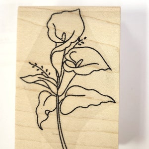 Könnte beinhalten: Ein Holzstempel mit einer schwarzen Linienzeichnung einer einzelnen Blume mit Blättern. Die Blume hat einen langen Stiel und drei Blütenblätter.