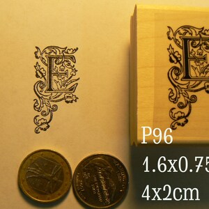May include: A wooden rubber stamp with a black and white design of a letter E with decorative flourishes. The stamp is labeled "P96" and measures 1.6x0.75 inches or 4x2 centimeters.