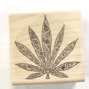 May include: A wooden stamp with a black and white paisley design of a marijuana leaf.