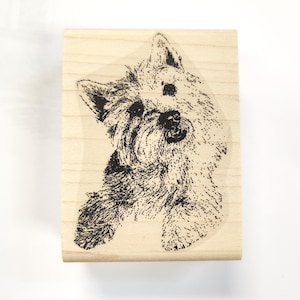 May include: A wooden rubber stamp with a black and white illustration of a dog's head. The dog is looking to the left and has a fluffy coat.