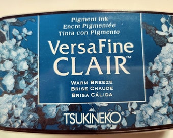 May include: A blue and silver ink pad with the text "VersaFine CLAIR" and "Warm Breeze, Brise Chaude, Brisa Cálida" in white. The ink pad is made by Tsukineko.