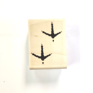 May include: A wooden block stamp with two black bird footprints. The footprints are facing downwards.