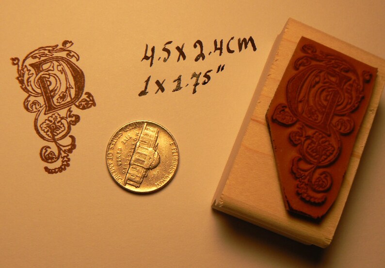 May include: A wooden stamp with a brown, intricate design of a letter "D" with floral accents. The stamp is 4.5 x 2.4 cm or 1 x 1.75 inches. A US penny is included for scale.