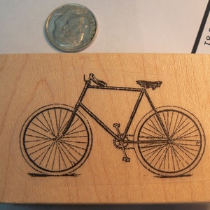 Pode incluir: Um carimbo de borracha de madeira com uma ilustração em preto e branco de uma bicicleta vintage.