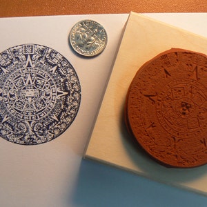May include: A 2-inch diameter rubber stamp with a detailed design of the Aztec calendar. The stamp is mounted on a wooden block.